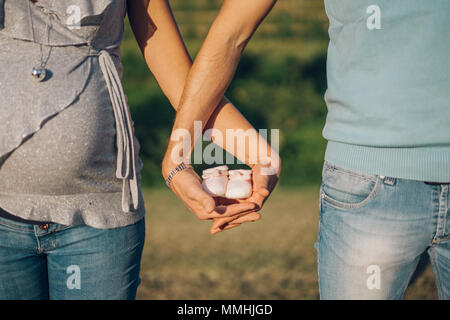 Couple is waiting for a child and holds a pair of pink woolen slippers in his entwined hands. Stock Photo