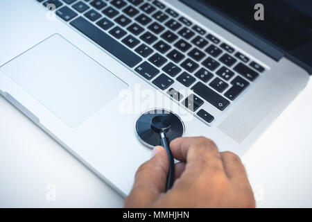 Man hand holding a stethoscope to check a laptop , concept of safety and protect computer from viruses and spyware Stock Photo