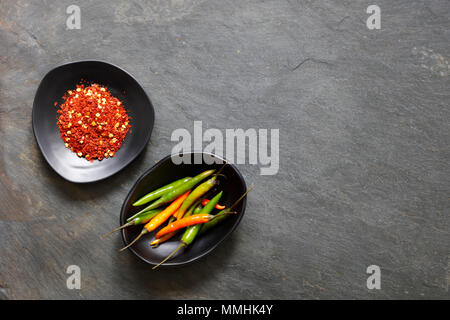 Ground dried chilli peppers with fresh peppers in black bowls with copy space Stock Photo