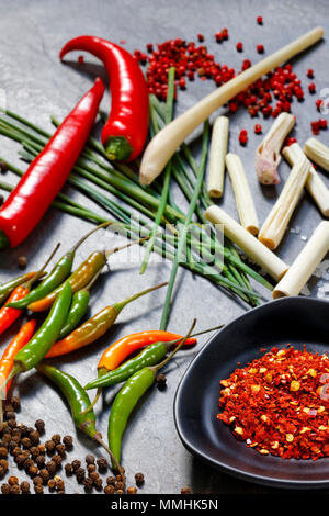 Ground dried chilli peppers with fresh peppers, lemon grass and chives on slate background Stock Photo
