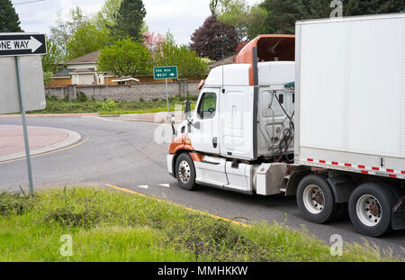 Low cab big rig white semi truck for long haul transportation and delivery carry dry van semi trailer and running on the local road circle intersectio Stock Photo