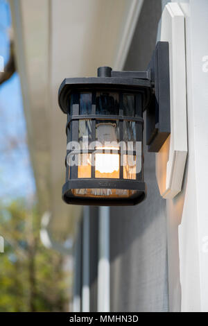 An outdoor wall light sconce with a low energy bulb lighting a house door Stock Photo