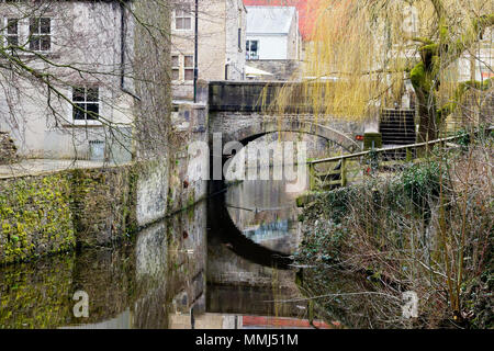 In Skipton the Leeds and Liverpool canal passes under a single arch bridge. Surrounding buildings are reflected in the canal surface. Stock Photo