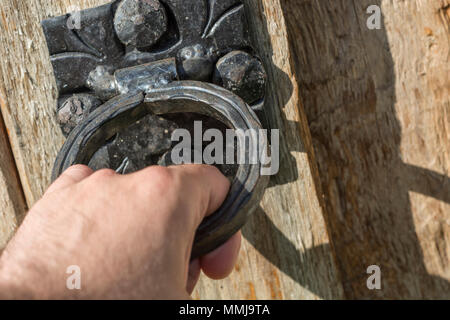 Male hand knock with old black door knocker on wooden and rustic door. Close up, selective focus Stock Photo