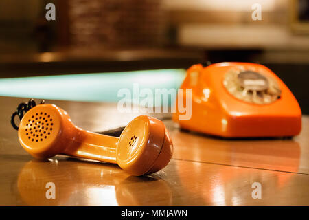 Handset of an orange telephone with dial placed on a wooden table inside a bar. Stock Photo