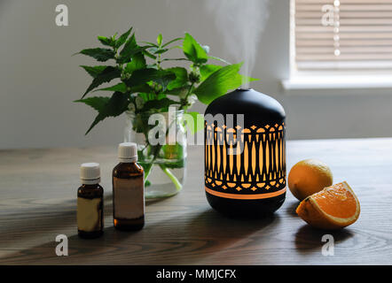 The ultrasonic aroma diffuser is made in oriental style. There are aromatic oils, lemon and a slice of orange near the diffuser on the table. Stock Photo