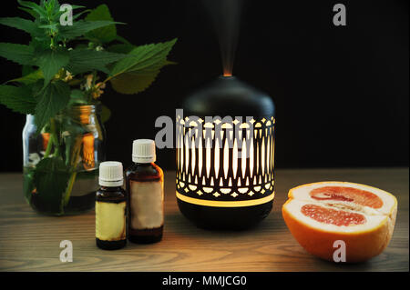 The ultrasonic aroma diffuser is made in oriental style. There are aromatic oils, half a grapefruit near the diffuser on the table. Stock Photo