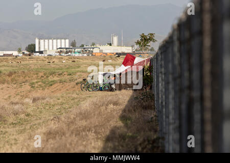 Homeless Camp agaist cyclone fence, dry grass, dry grass, field containing drainage, bicycles used for transportation. Stock Photo