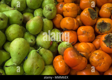 Green pears and orange persimmon, food background of fresh fruits. Stock Photo