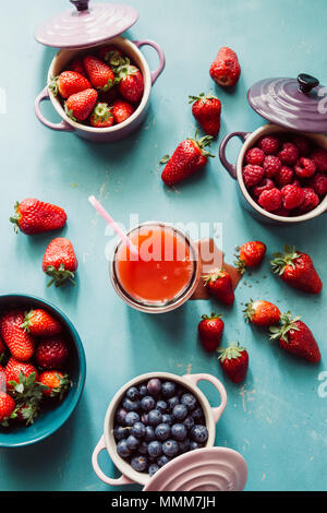 Summer fruit background, top view of berries inside ceramic colored cocotte, blueberries, strawberries, raspberries, flat lay, blue table, wth a glass Stock Photo