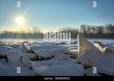 A beautiful snowy winter sunrise along the frozen Maumee River in Northwest Ohio. Huge chunks of broken ice have been pushed up on the shore.