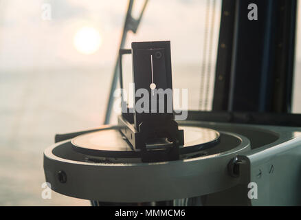 Close up of nautical marine magnetic compass on yacht or boat with beautiful sunrise on background. Calculation of compass error taking bearing from s Stock Photo