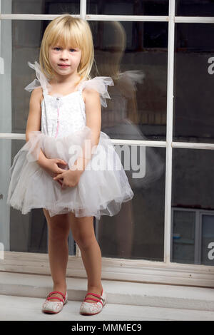 Girl 3 years old in a beautiful white dress near the winter window Stock Photo