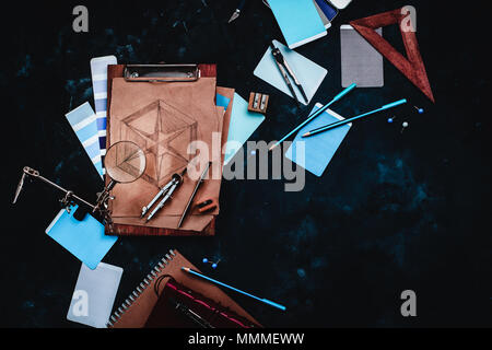 Draftsman or designer workplace with craft paper, sketches, compasses, rulers, clipboards and pencils on a dark stone background. Top view with copy s Stock Photo