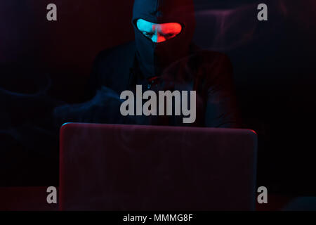 Angry computer hacker in suit stealing data from laptop illuminated by red and blue light Stock Photo