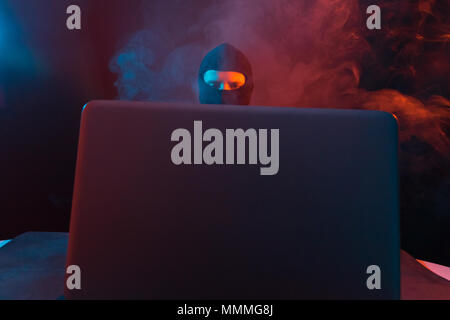Angry computer hacker in suit stealing data from laptop illuminated by yellow and blue light Stock Photo
