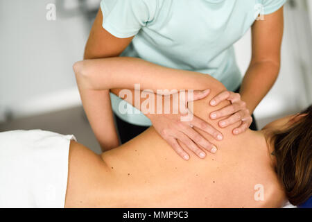 Professional female physiotherapist giving shoulder massage to brunette woman in hospital. Medical check at the shoulder in a physiotherapy center. Stock Photo