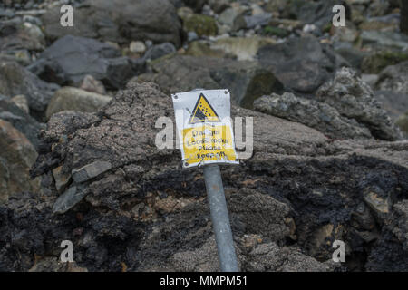 Danger loose rocks sign which has been bent and is falling over against some loose rocks on the coast at Newlyn in Cornwall Stock Photo
