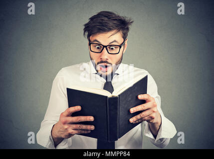 Bearded handsome man in glasses reading book and stunned with new things learned having shocked face expression. Stock Photo