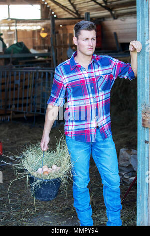handsome blond man at a barn holding a basket with eggs Stock Photo