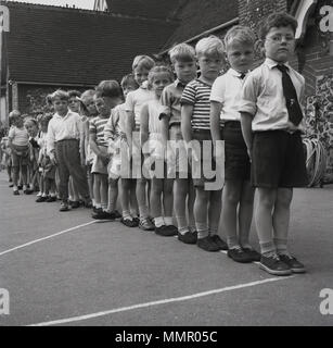 1950s, historical, group of junior or primary school children line up, feet together, hands by the side, outside in a playground, England, UK. Lining up, quietly and safely, is an important discipline for pupils in an elementary school, as it something that is required several times during the day, for example. to enter lessons, at lunchtime and on leaving the school. Stock Photo