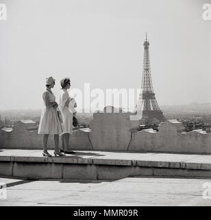 1950s, historical picture by J Allan Cash showing two elegant well-dressed French ladies standing on a tall building, looking over the skyline of the city of Paris and the iconic Eiffel Tower in the distance. Stock Photo