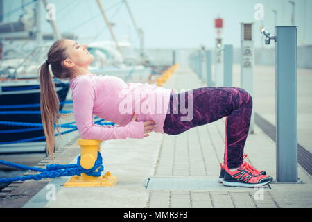 Vintage photo, Slim sporty girl wearing sports wear and exercising or stretching in seaport, concept of healthy and active lifestyle on fresh air Stock Photo