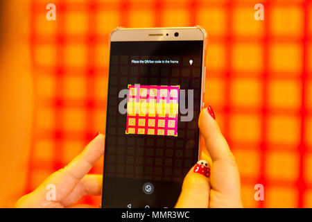 A lady hand holding a mobile smart phone to scan QR code on the wall Stock Photo