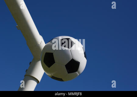 A black and white leather football at the cross of the goal posts Stock Photo