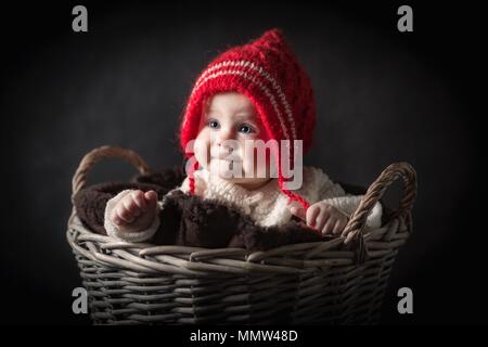 Beautiful baby girl in big basket portrait. Girl in red hat. Studio shot of 6 month old baby. Stock Photo