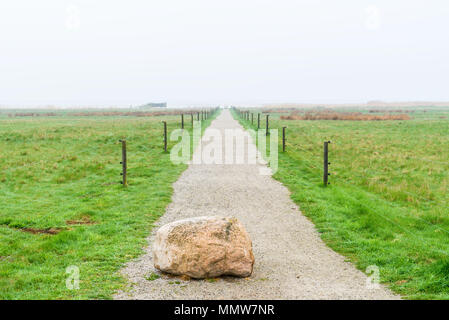 Jaravallen nature reserve in Skane, Sweden - Granite boulder used as a traffic barrier on gravel road into misty coastal landscape with bird tower vis Stock Photo