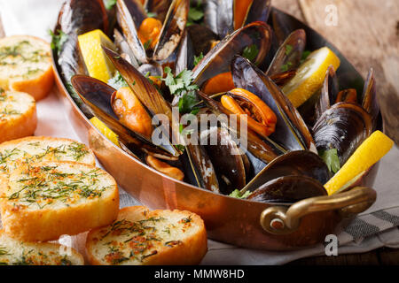 French mussels with lemon, parsley and garlic close-up in a copper pot and toast on the table. horizontal