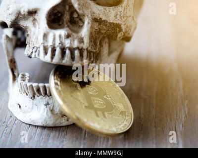 Close up of Skull biting Golden bitcoin on wooden table. The concept of investment and Fluctuation of bitcoin and cryptocurrency. The feeling of disap Stock Photo
