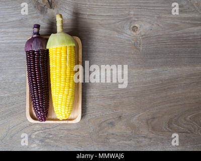 The corn stalks boiled and delicious on the wooden dish and the dish on wooden table. The color of corn is yellow and brown. copy space for text Stock Photo