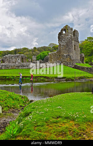 A young couple carefully cross the famous stepping stones over the  Ewenny river where it passes Ogmore Castle, nr Bridgend, South Wales Stock Photo