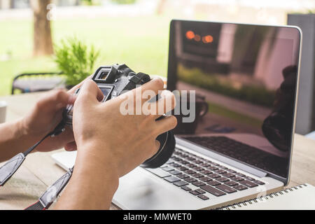 Man hands hand holding camera and using laptop computer in coffee shop. Stock Photo
