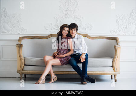 Handsome man is listening to his beautiful pregnant wife's tummy and smiling Stock Photo