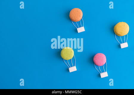 Colorful macarons and sugar cubes in form of hot air balloons against blue sky background minimal creative concept. Space for copy. Stock Photo