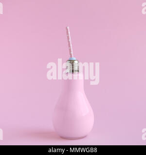 Small bottle in form of light bulb full of fruit yogurt with drinking straw against pastel pink background. Stock Photo