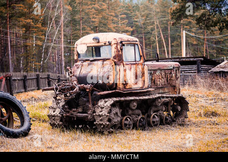 Close-up of an old rusty tractor with a broken door and no wheels on the background of a green coniferous forest Stock Photo