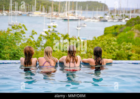 Antigua Lesser Antilles islands in the Caribbean West Indies - Four young women enjoy an infinity swimming pool view overlooking English Harbour Stock Photo