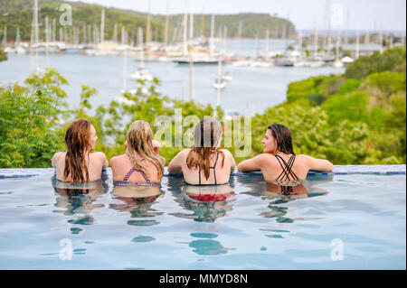 Antigua Lesser Antilles islands in the Caribbean West Indies - Four young women enjoy an infinity swimming pool view overlooking English Harbour Stock Photo