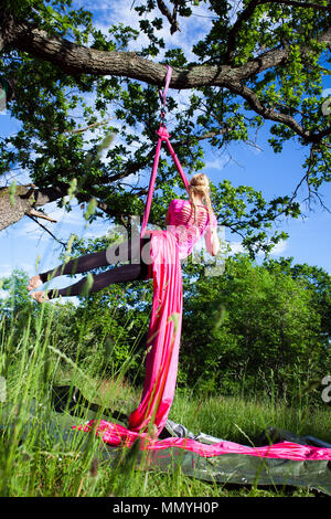 Young aerialist in an outdoor environment with pink silk hanging from a tree in summertime Sweden. Stock Photo