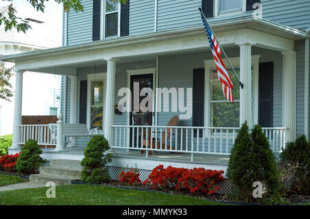 A typical front porch of a home in a small town in the U.S.A. Featuring an American flag proudly flying and a porch swing to enjoy the spring day. Stock Photo