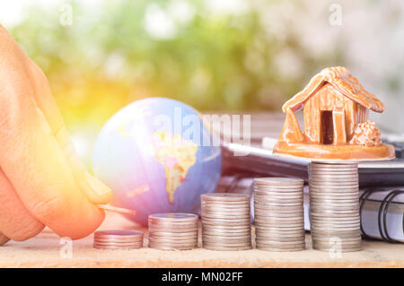 hand put money  on pile of coins, globe and house, concept in growth, sell, buy, save and investt in business of home around the world Stock Photo