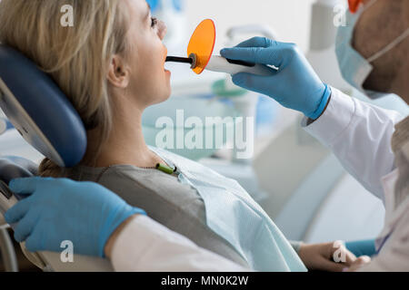 Crop man in gloves using ultraviolet to make filling of tooth to young client healing oral cavity. Stock Photo