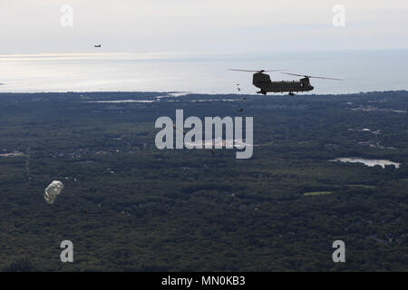 A team of paratroopers jump out of a CH-47 Chinook Helicopter over Castle drop zone during Leapfest 2017 at the University of Rhode Island, West Kingston, R.I., Aug. 6, 2017. Leapfest is the largest, longest standing, international static line parachute training event and competition hosted by the 56th Troop Command, Rhode Island Army National Guard to promote high level technical training and esprit de corps within the International Airborne community. (U.S. Army photo by Pfc. Lucas Wenger) Stock Photo