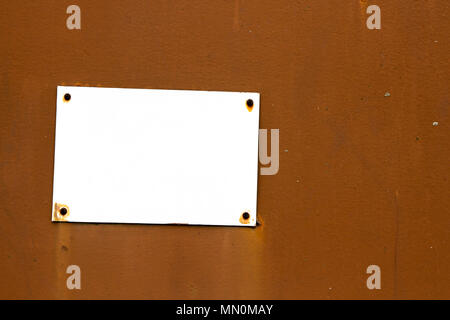 Empty rusty and grungy white signboard in rectangular shape weathered under the elements and fixed to an old brown wooden wall with rusty nails. Negat Stock Photo