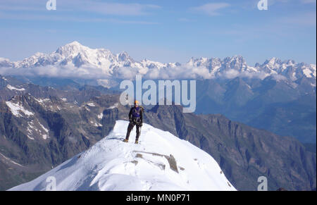 male mountain climber on the summit of Gran Paradiso with a great view of Mont Blanc behind him Stock Photo