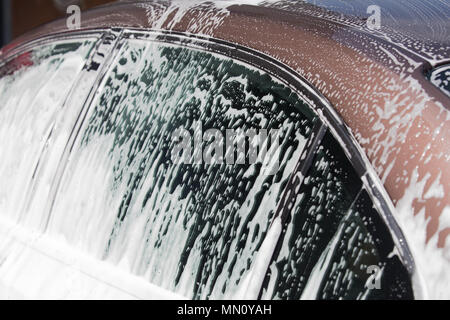 Car in washing service. White foam flowing on car windows. Stock Photo